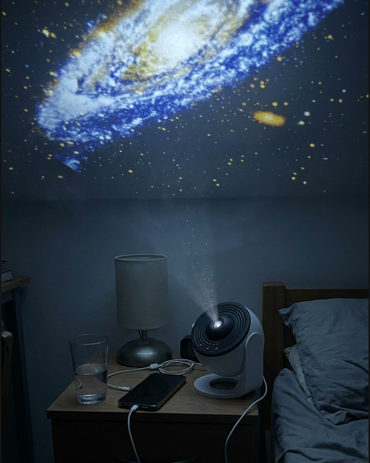 Lunora galaxy projector on a nightstand projecting a galaxy on the bedroom ceiling